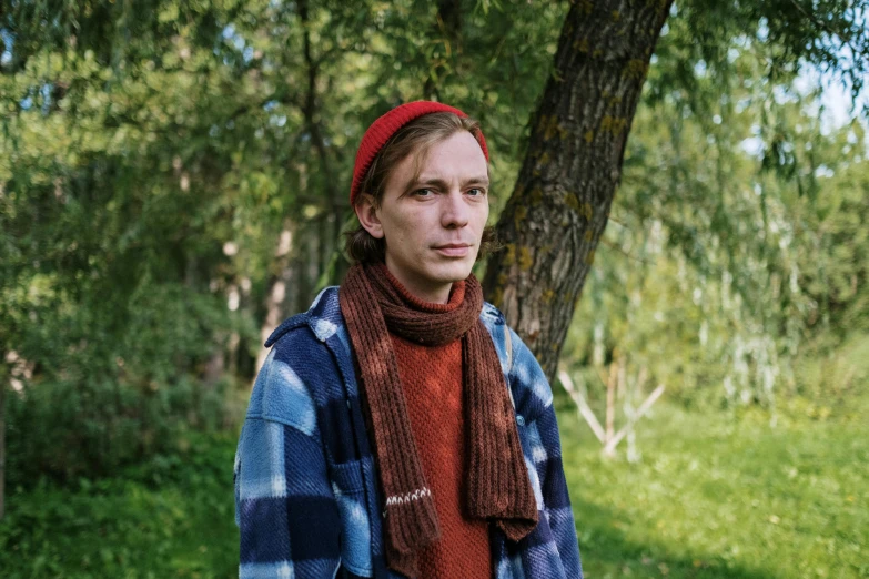 a young man in a plaid jacket, scarf and red hat looking into the distance