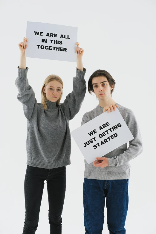 two people are holding signs and standing with their hands raised