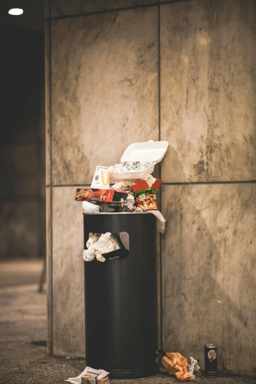 a trash can full of various items and garbage near a wall