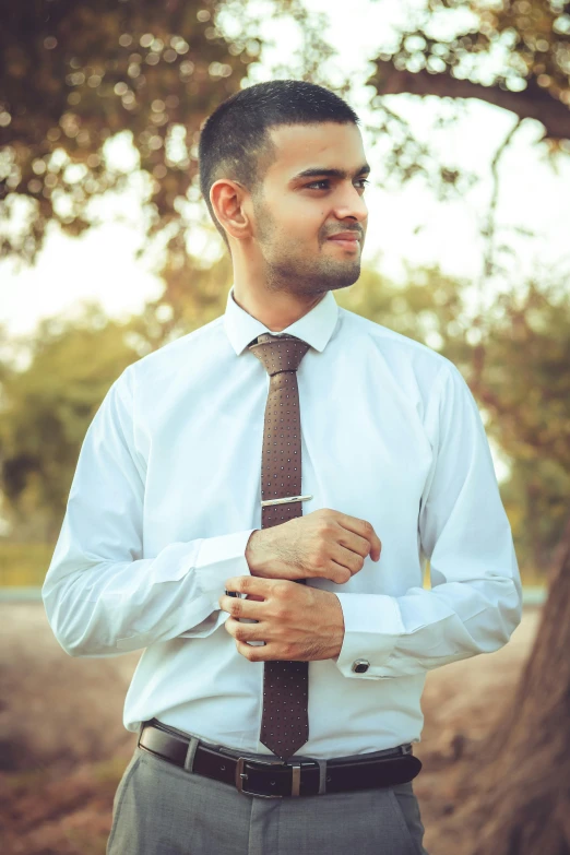 man adjusting his tie near some trees