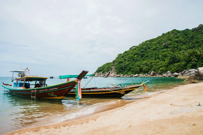 two boats are parked along the shore next to a hill