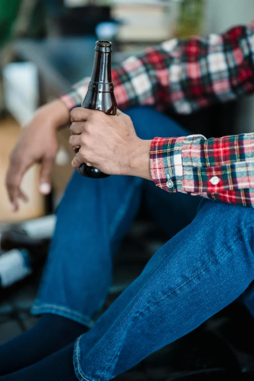 a person holding a beer bottle sitting on the ground