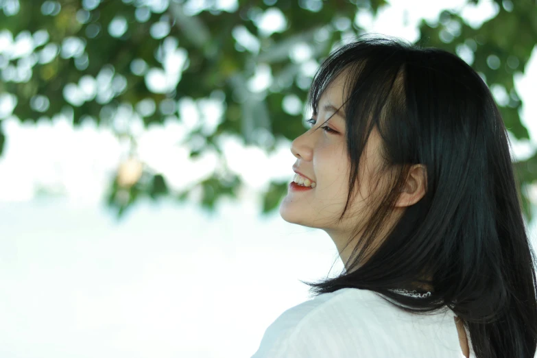 an asian girl smiles while standing under a tree