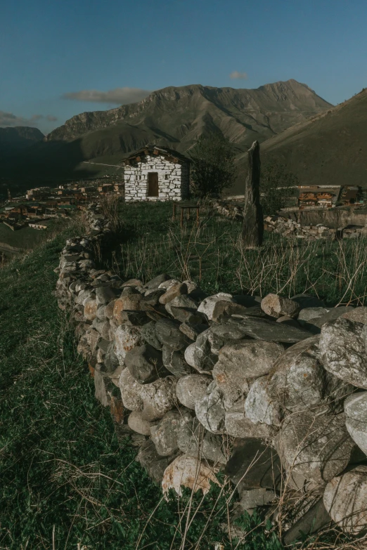 a stone wall with rocks along side of it in front of mountains