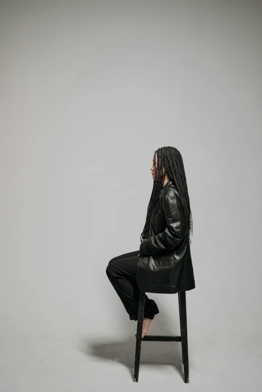 a woman sitting on top of a wooden chair in front of a white wall