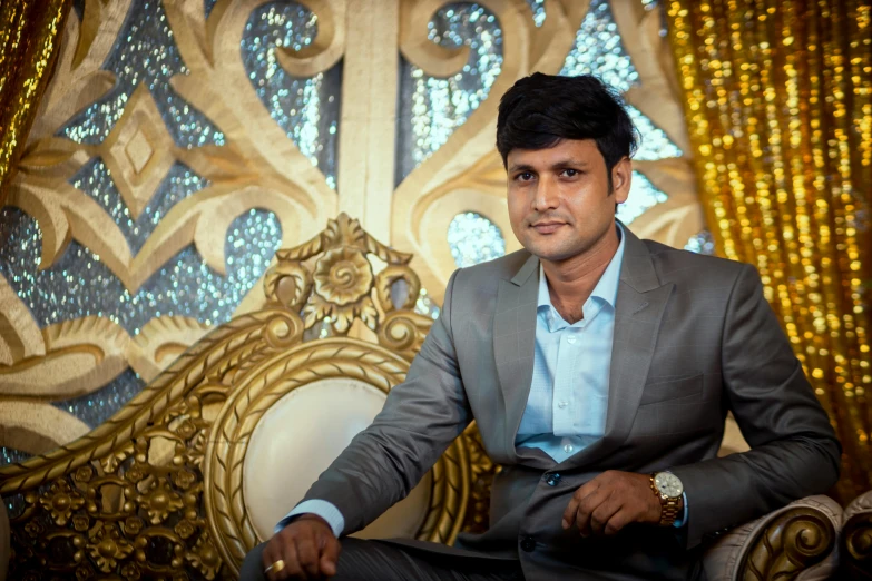 an indian man sitting in front of a gold curtain