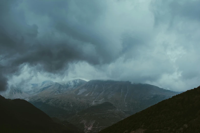 a mountain with dark skies, clouds and some green grass