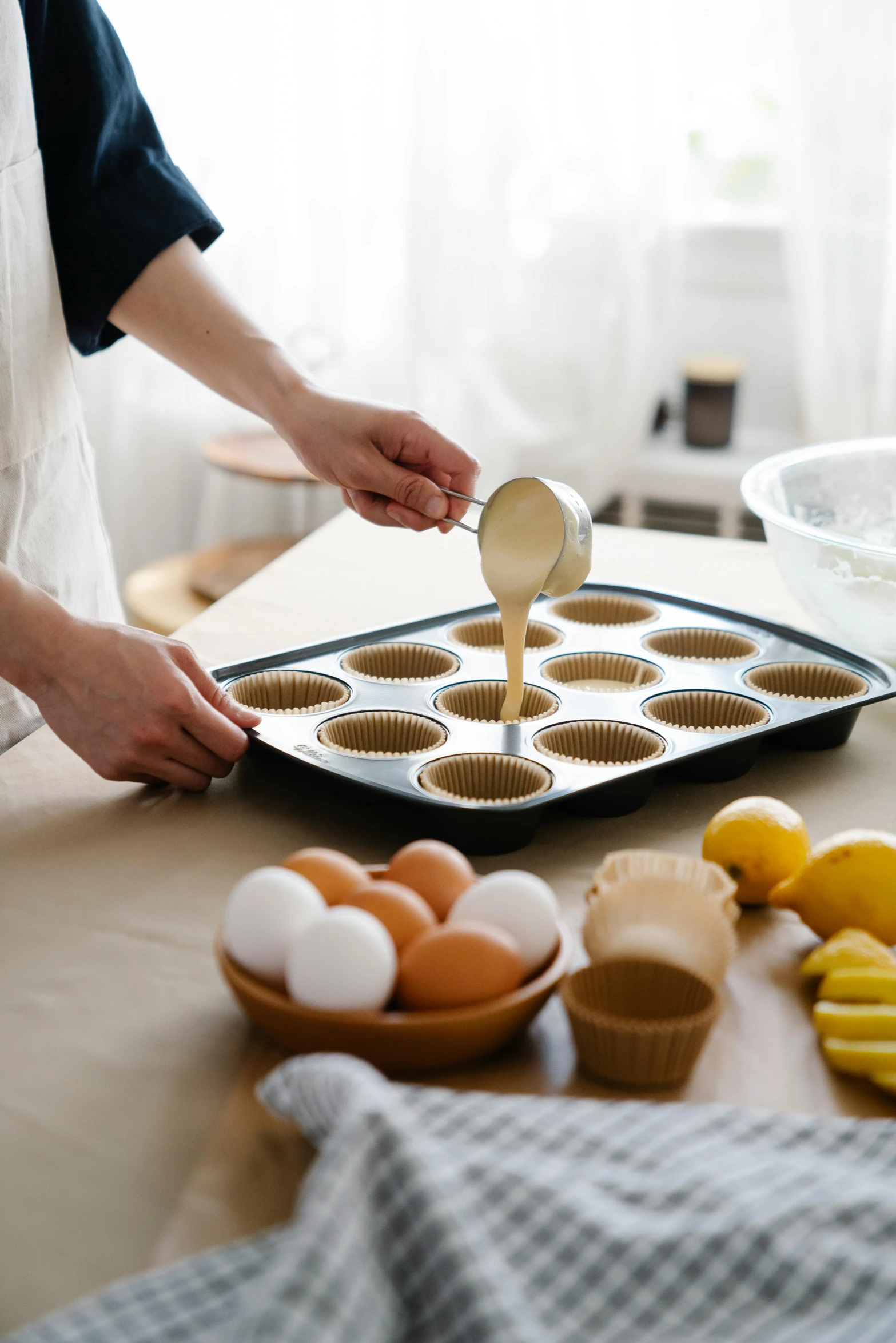 a woman spooning batter onto a pan filled with muffins