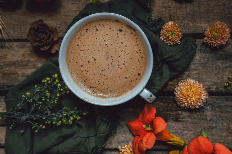 a white cup on a table with flowers and other flowers