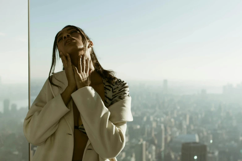 a young woman wearing a white jacket looks up while she stands outside the window