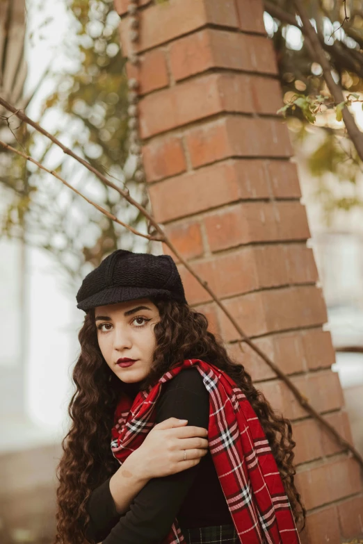 a young lady dressed in plaid sitting by a brick building