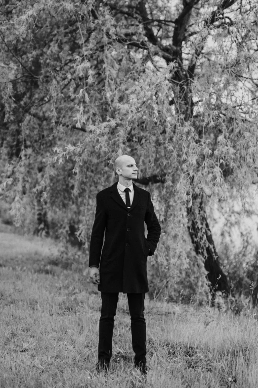 man in coat and tie standing in field with trees in background
