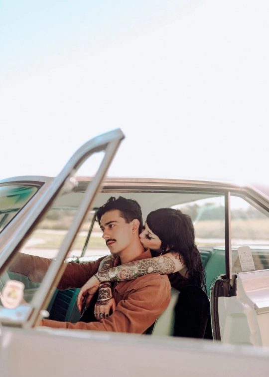 a woman sits in the passenger seat of an old fashioned car and a man is holding onto her while sitting in the driver's seat