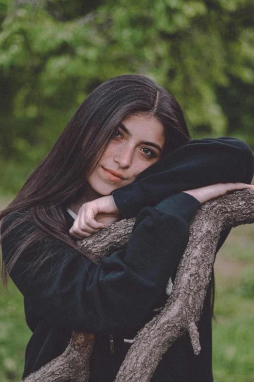 a woman wearing a black coat leaning on a tree nch