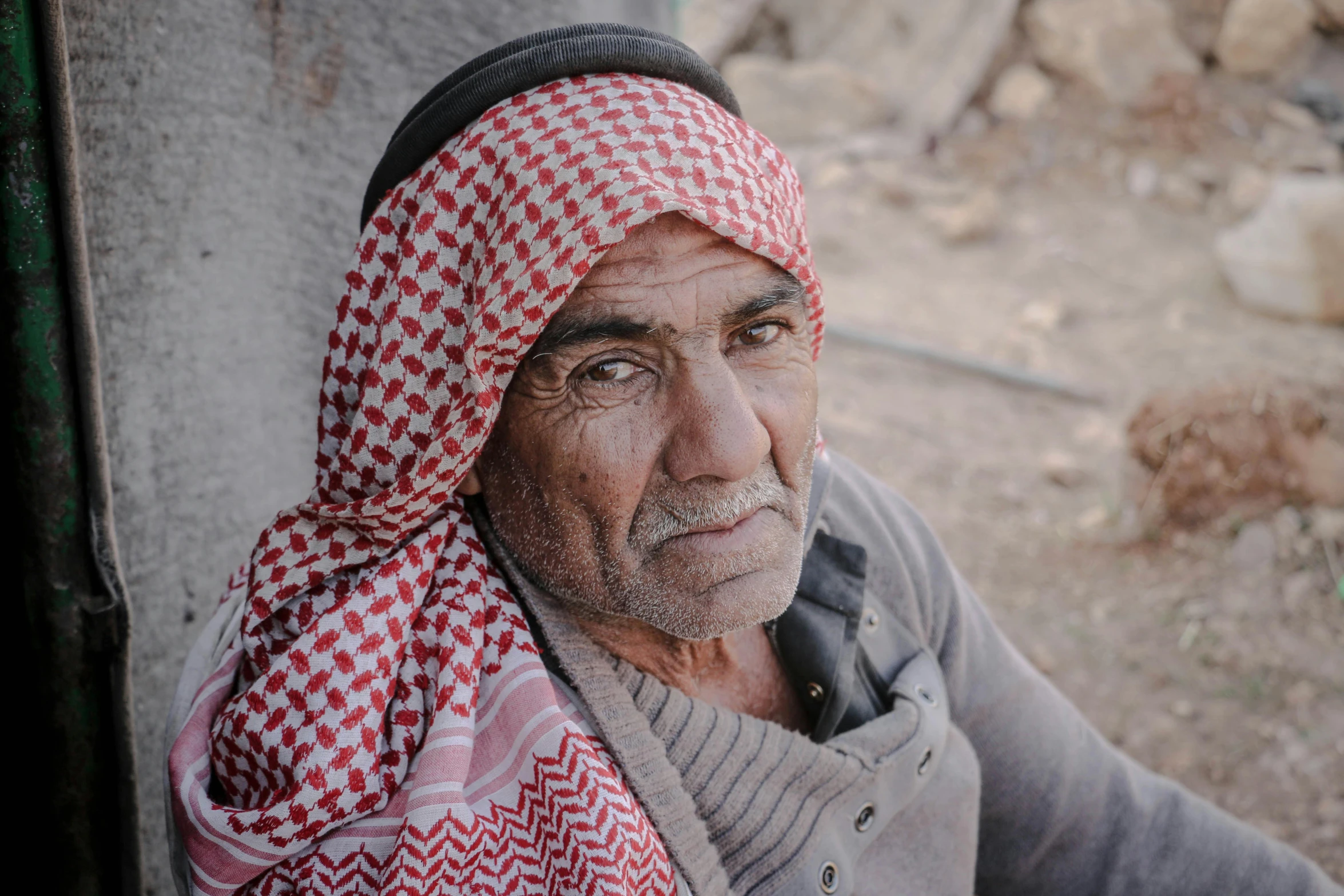 a man in a red and white headscarf looks off into the distance