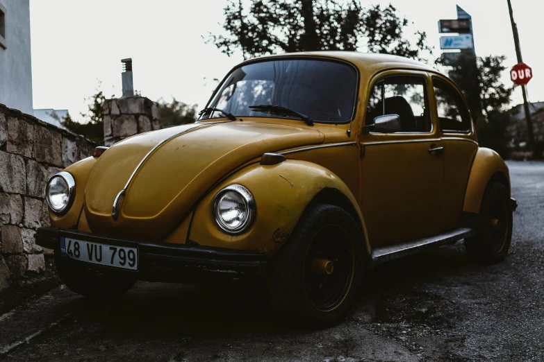 yellow vw bug parked in the street next to a stone wall