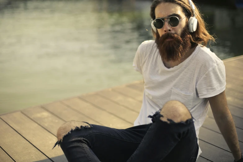 a man wearing headphones is sitting on a pier near the water