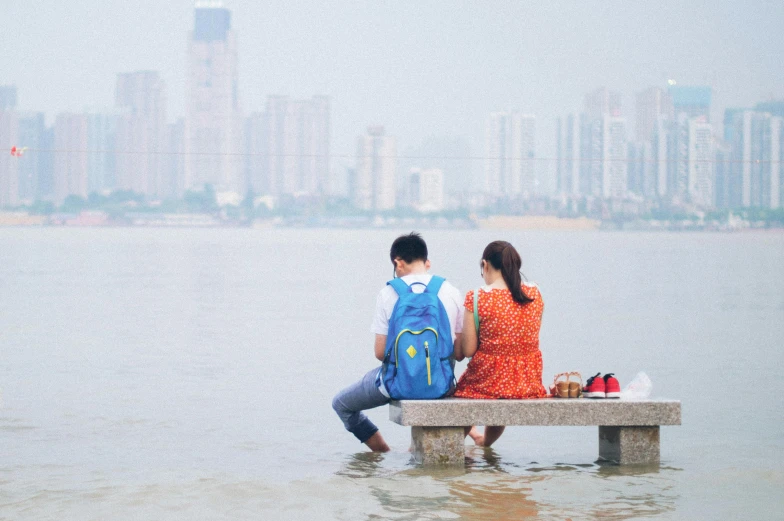 two people sitting on the pier with backpacks looking out at water