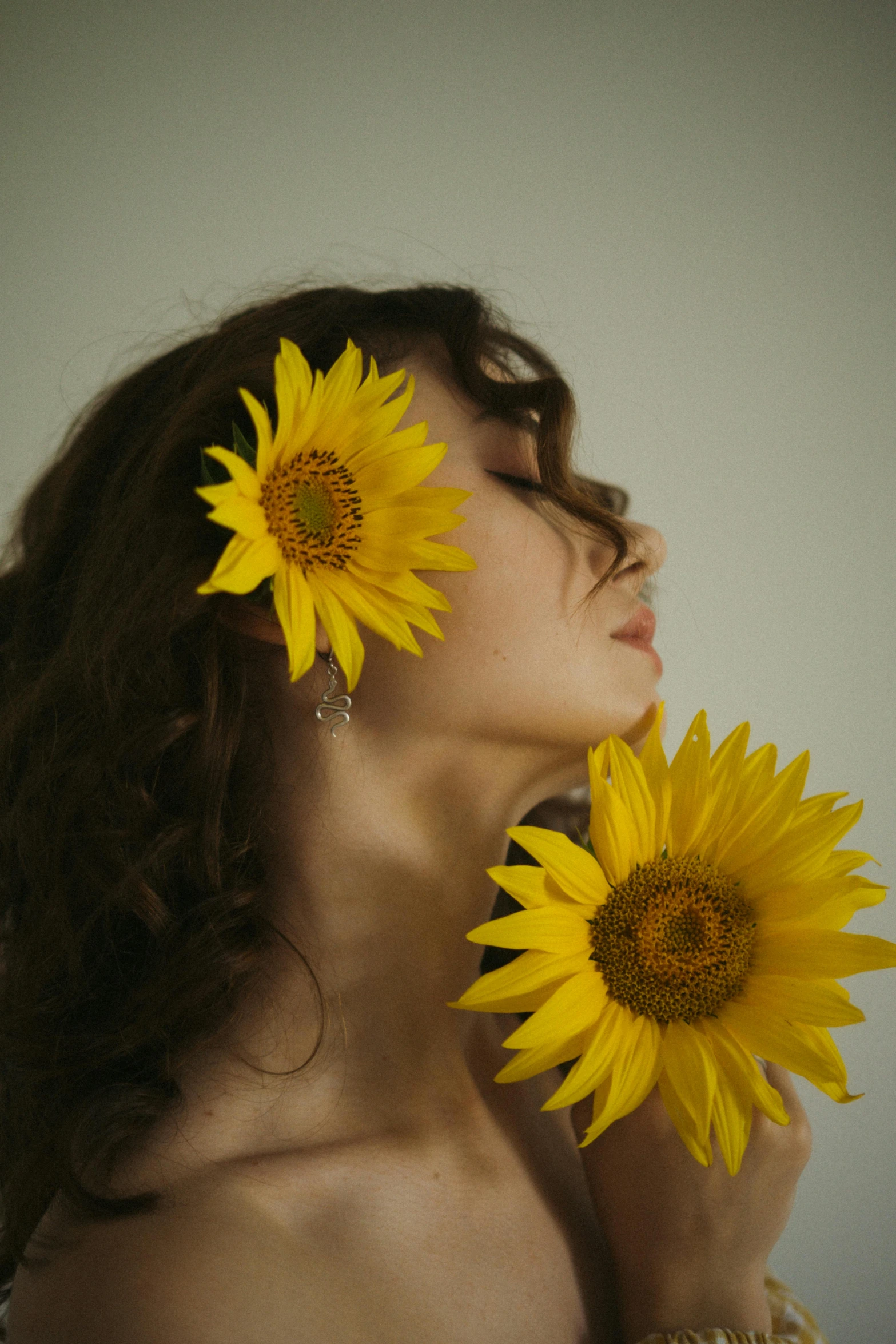 woman in brown dress holding up yellow sunflowers to her face