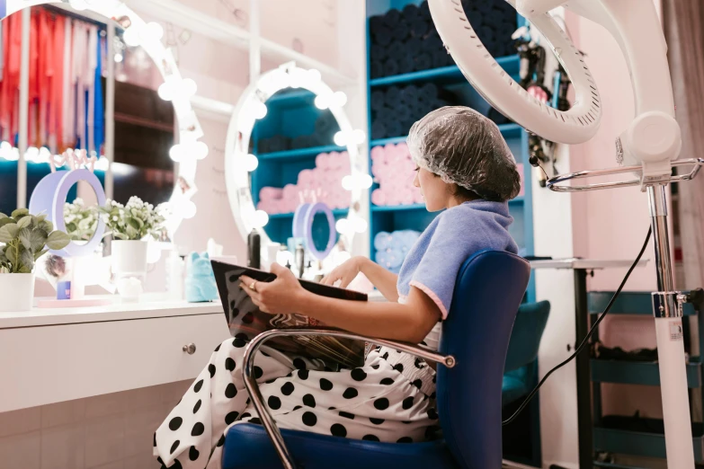 a woman sits in her salon chair and uses her laptop