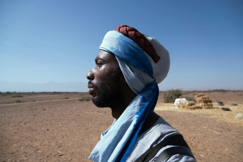 a man wearing a hat and a blue cloth is standing in the desert