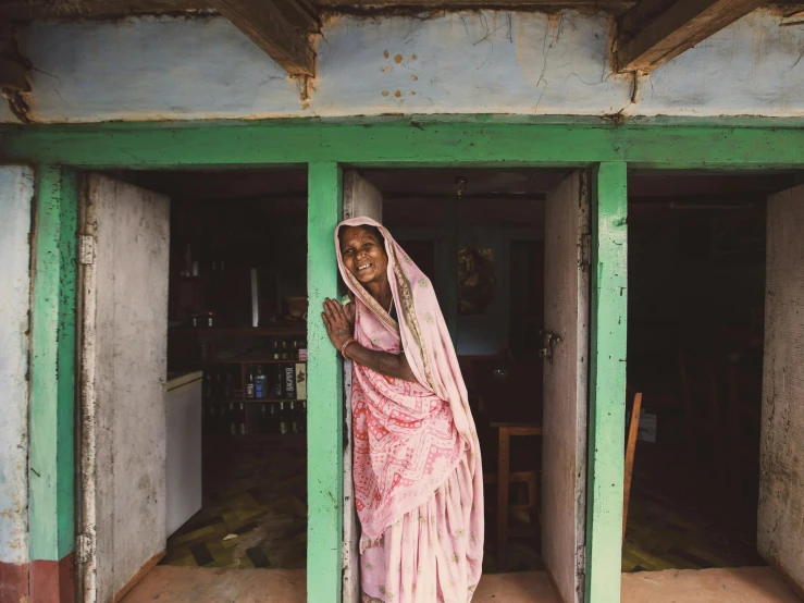 a woman in a pink sari standing outside of a wooden building