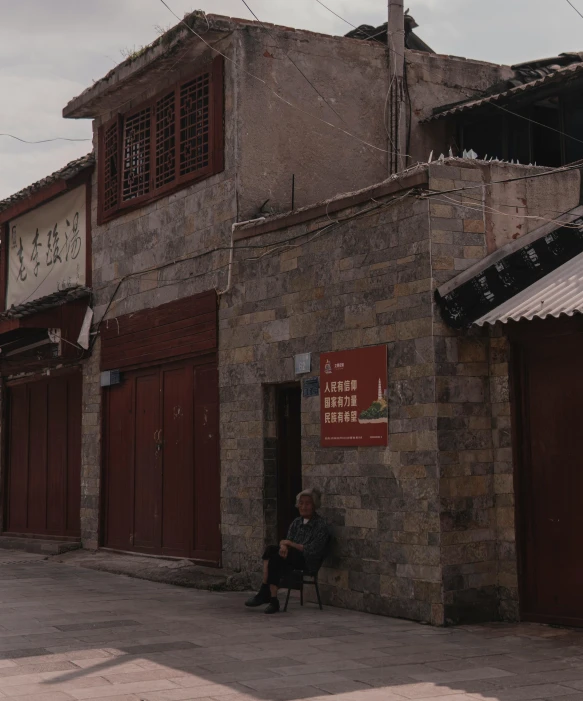 a man sitting on a bench in front of a building with a clock on the side