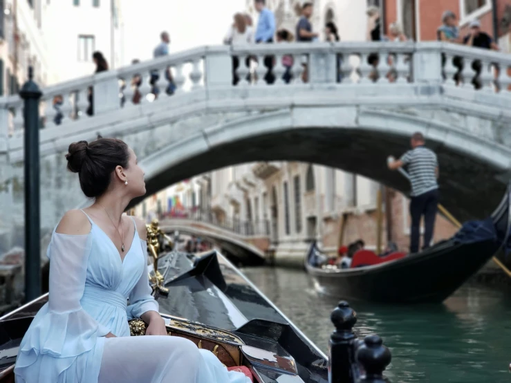 there is a lady sitting in a gondola near a bridge