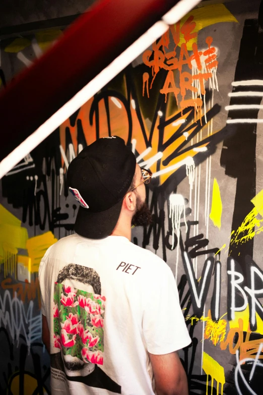 a man in a white shirt stands against a graffiti - wall