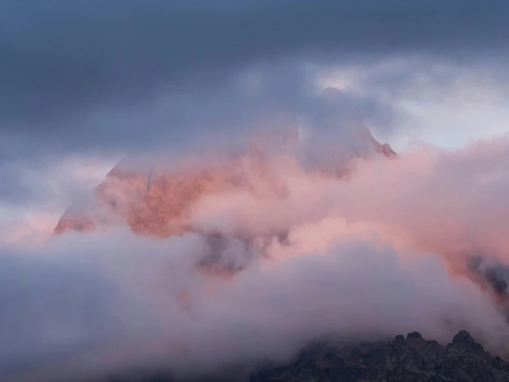 a bunch of clouds rising behind a mountain peak