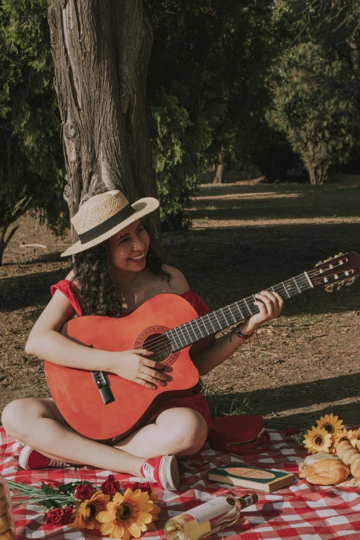 the girl is sitting under the tree playing the guitar