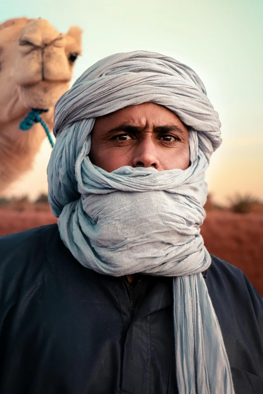 a man in blue headdress holds a camel's head