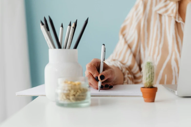 a person in a striped shirt writing in a notebook next to cactus and cactus plant