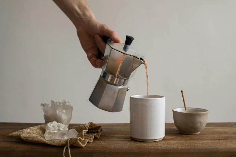 coffee being poured into white cups sitting on a wooden table