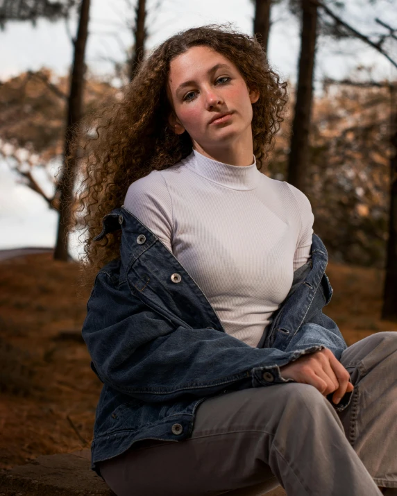 a woman sitting in the woods wearing a jean jacket