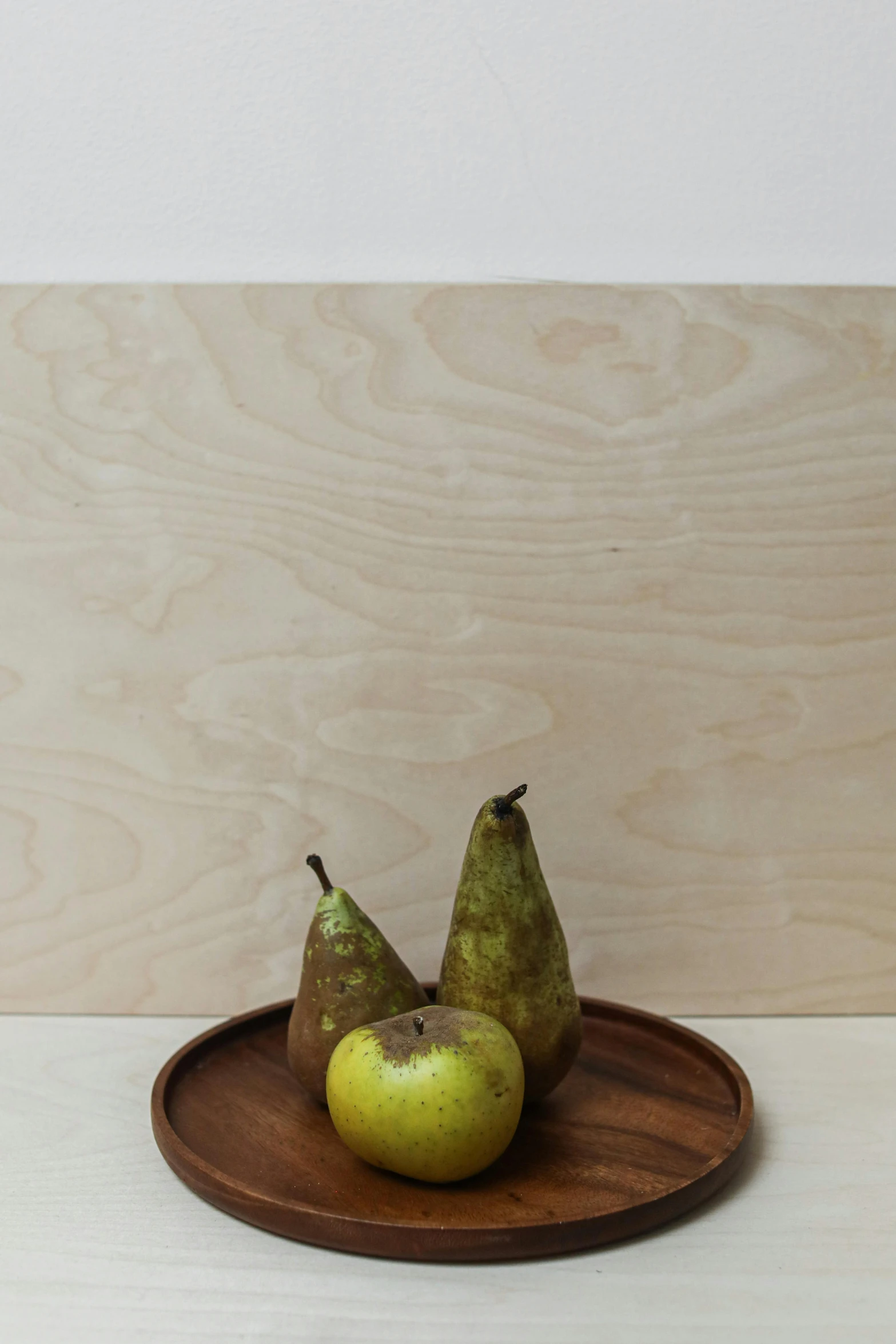 three pears and one green apple sit on a wooden plate