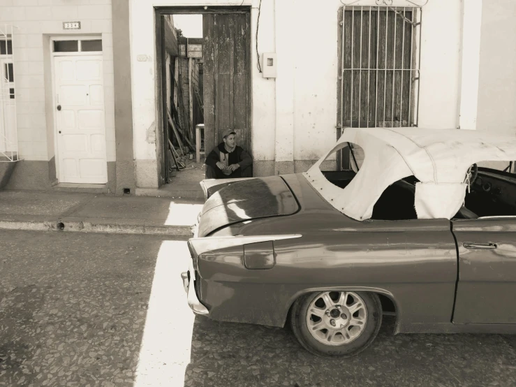 a man looking at a car with a tarp over it's hood