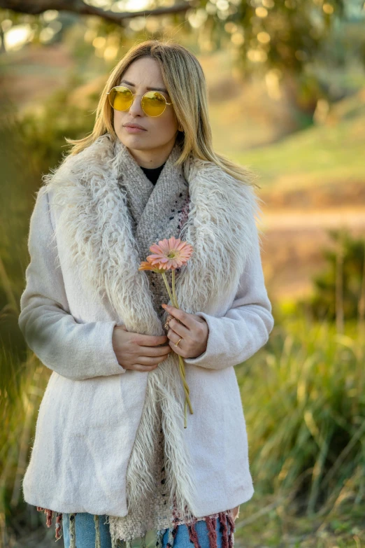 the woman is standing in a field wearing a fur coat