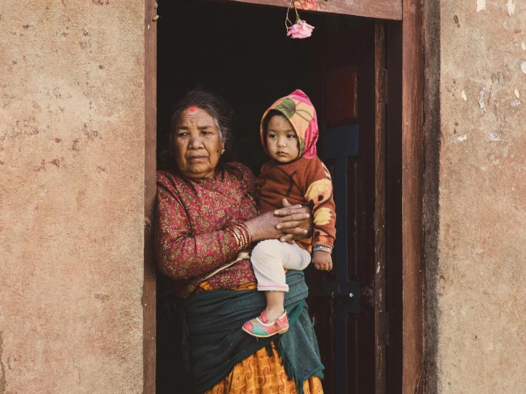 a woman holding a baby in front of her doorway