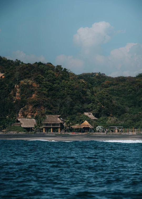 a beach with mountains and houses on the hill behind