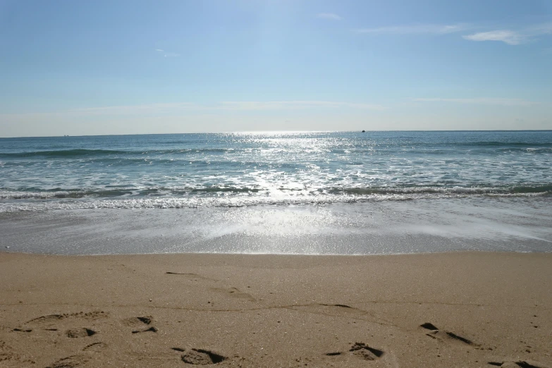 a beach with waves, clear blue water and some footprints in the sand