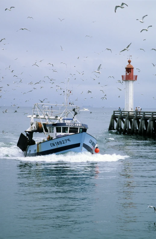 a blue boat traveling across the ocean next to a light house