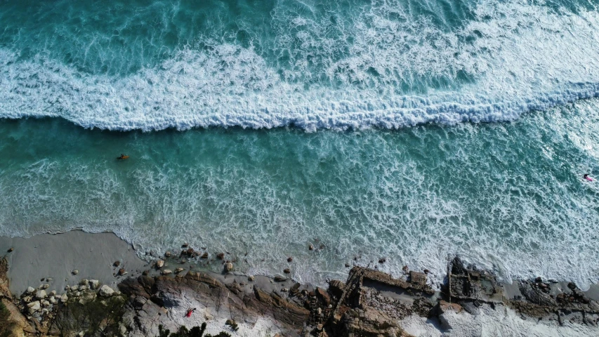 view from above of ocean with people swimming and standing on rocks