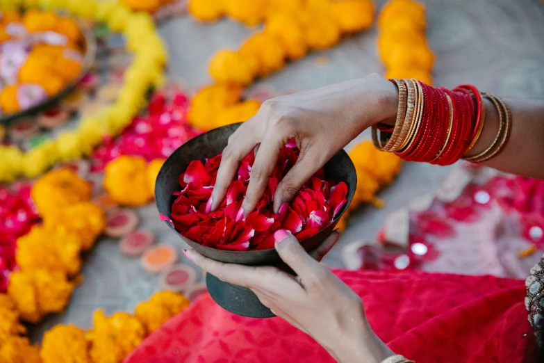 person touching red petals in a bowl with gold celets