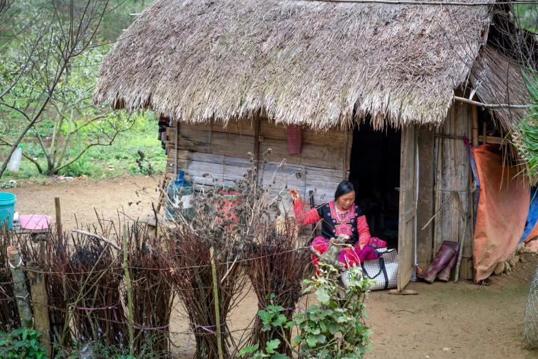 the woman sitting on the porch is next to a straw hut