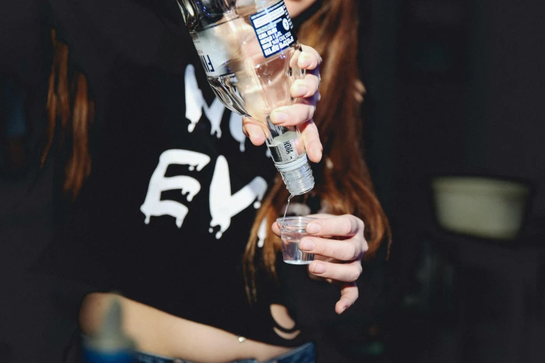 a woman is drinking from a cup, while holding a bottle