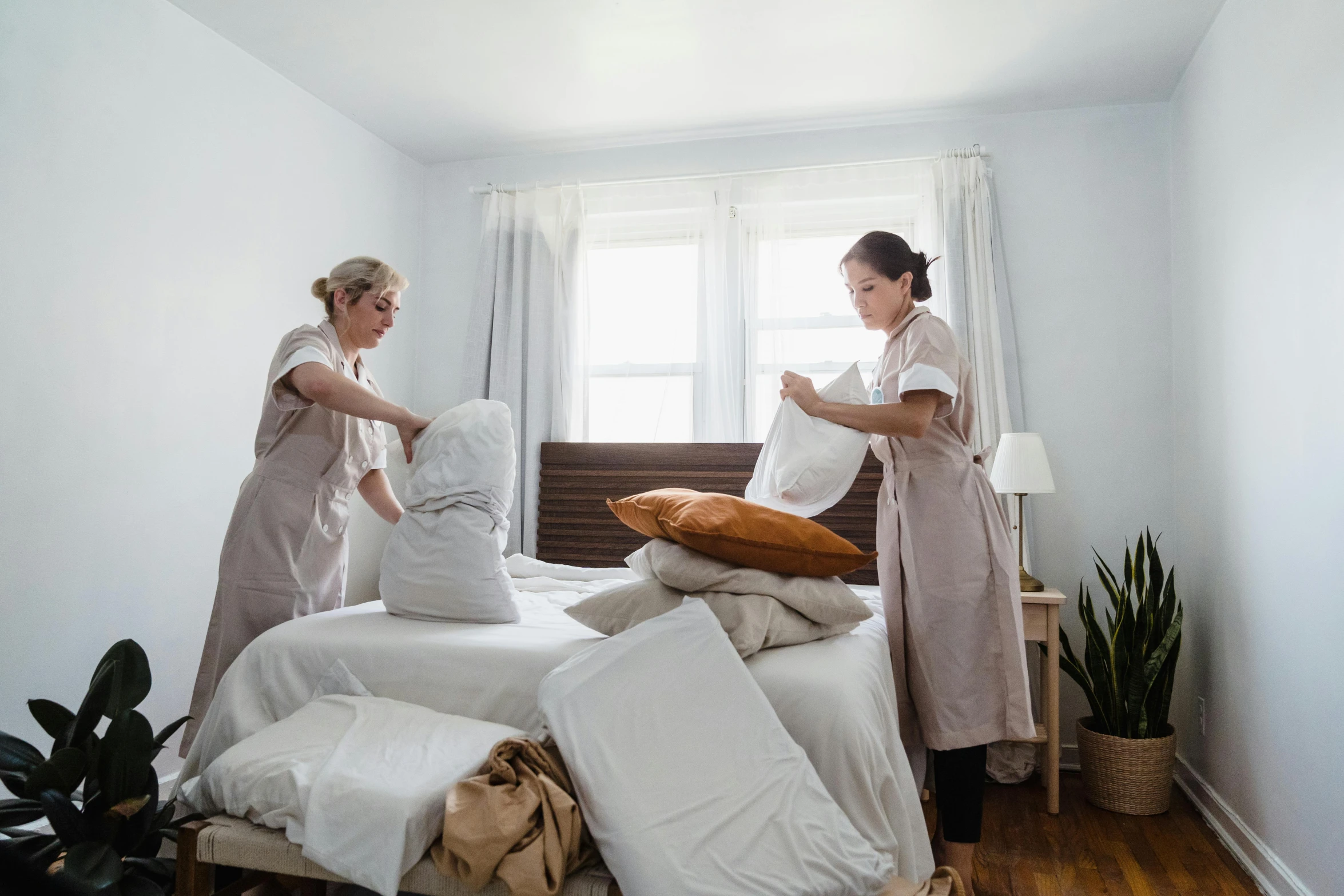 two women prepare to set up pillows on a bed