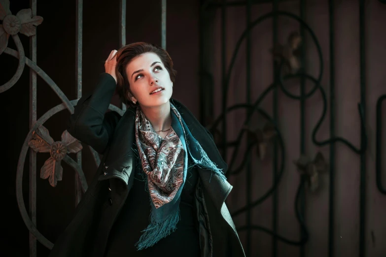 a woman in a dress and jacket poses near a metal fence