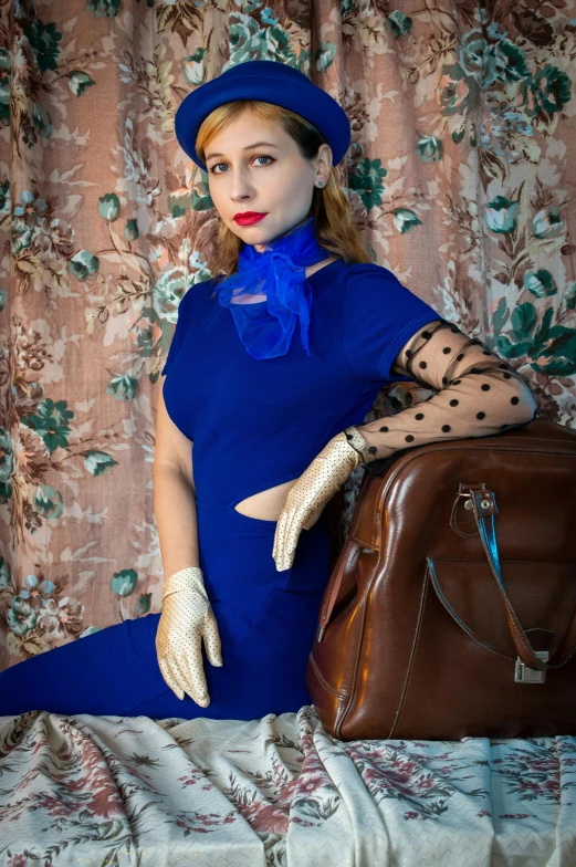 woman sitting on bed with suitcase and hat on head