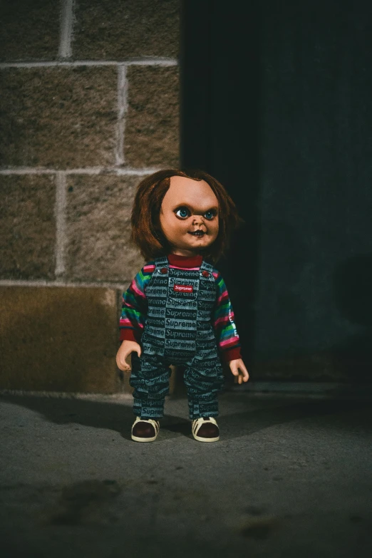 a creepy doll standing next to a brick wall